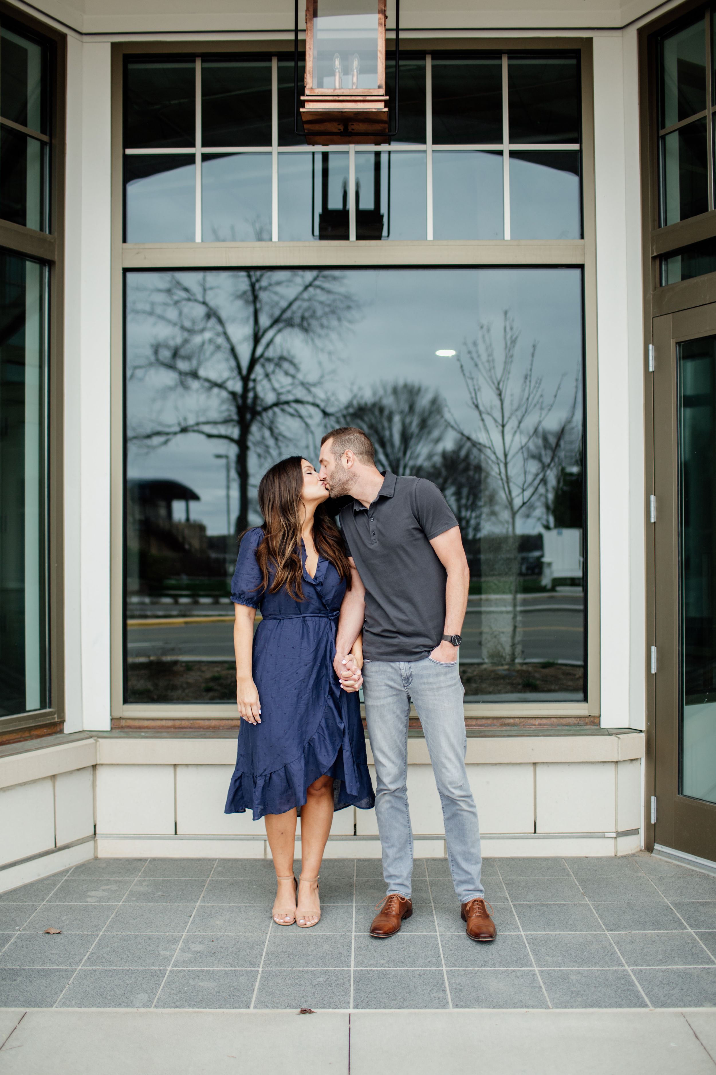 Couple sharing romantic moments in front of a modern building with large glass windows.