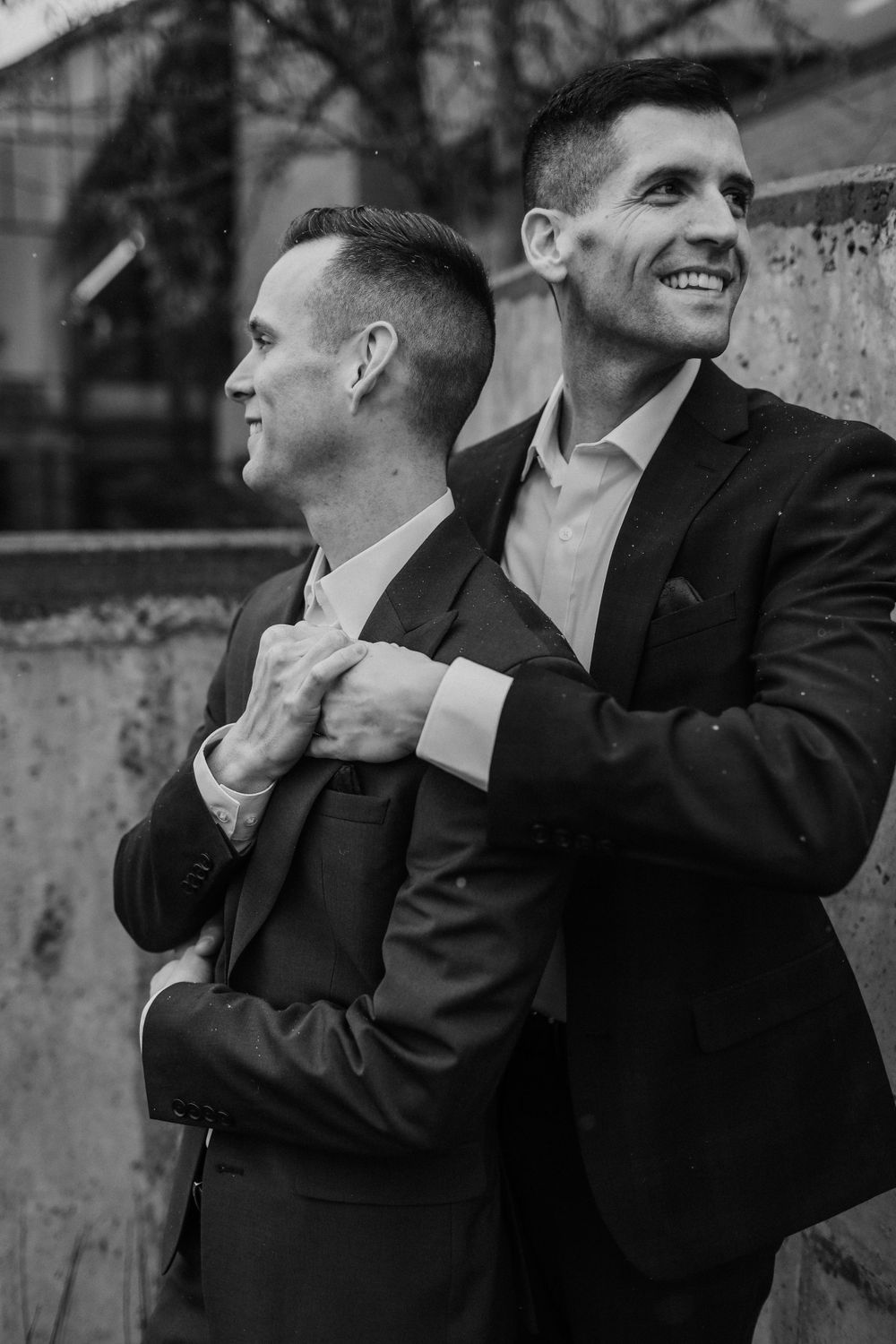 Black and white portrait of two men in suits embracing outdoors.