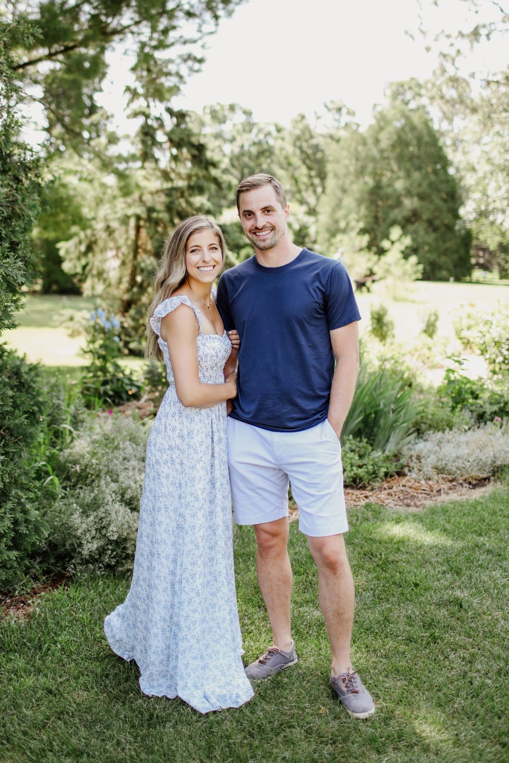 Couple in summer outfits standing together in sunny garden setting.