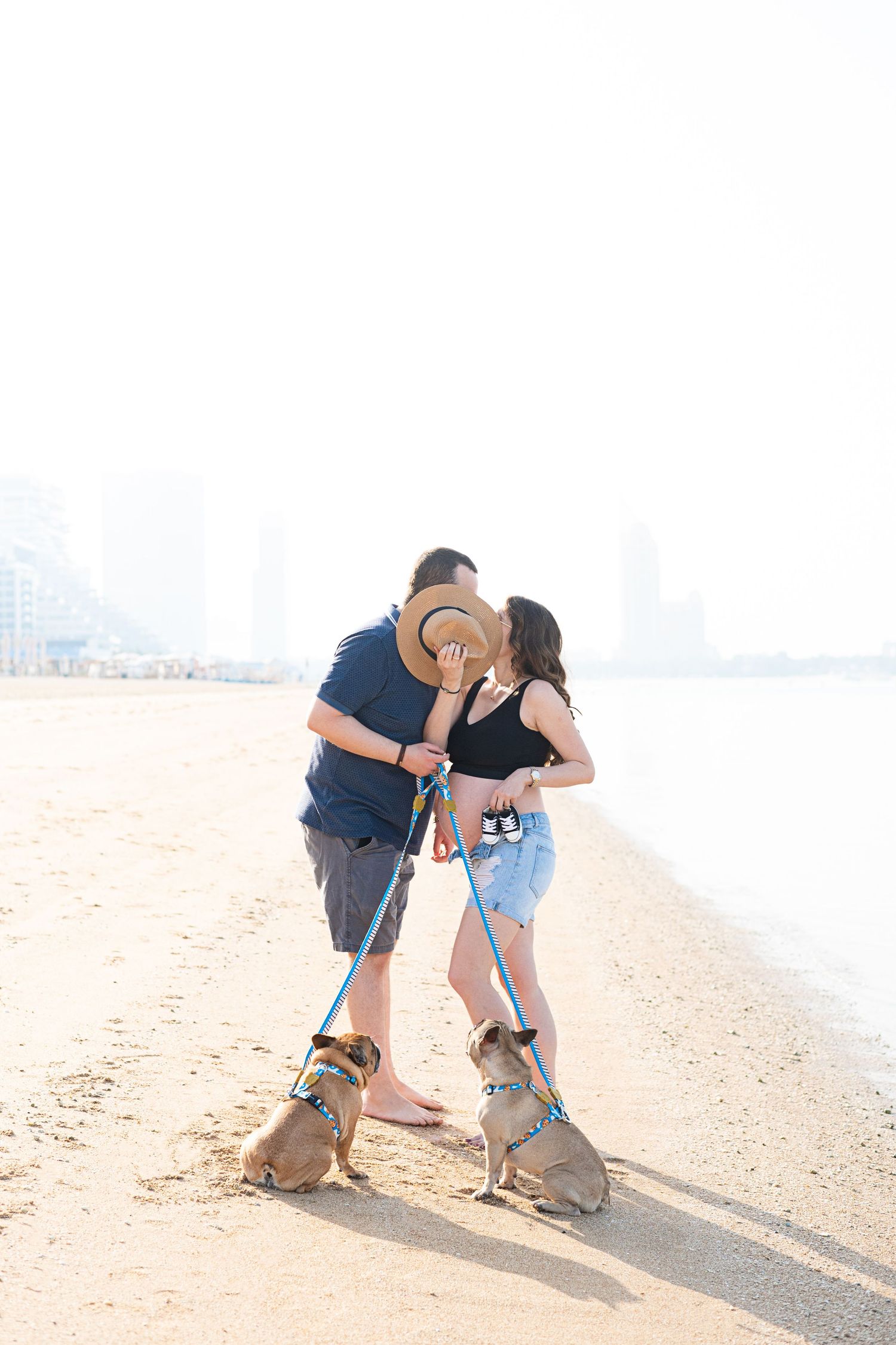 Couple sharing romantic moment on beach with two dogs playing at their feet.