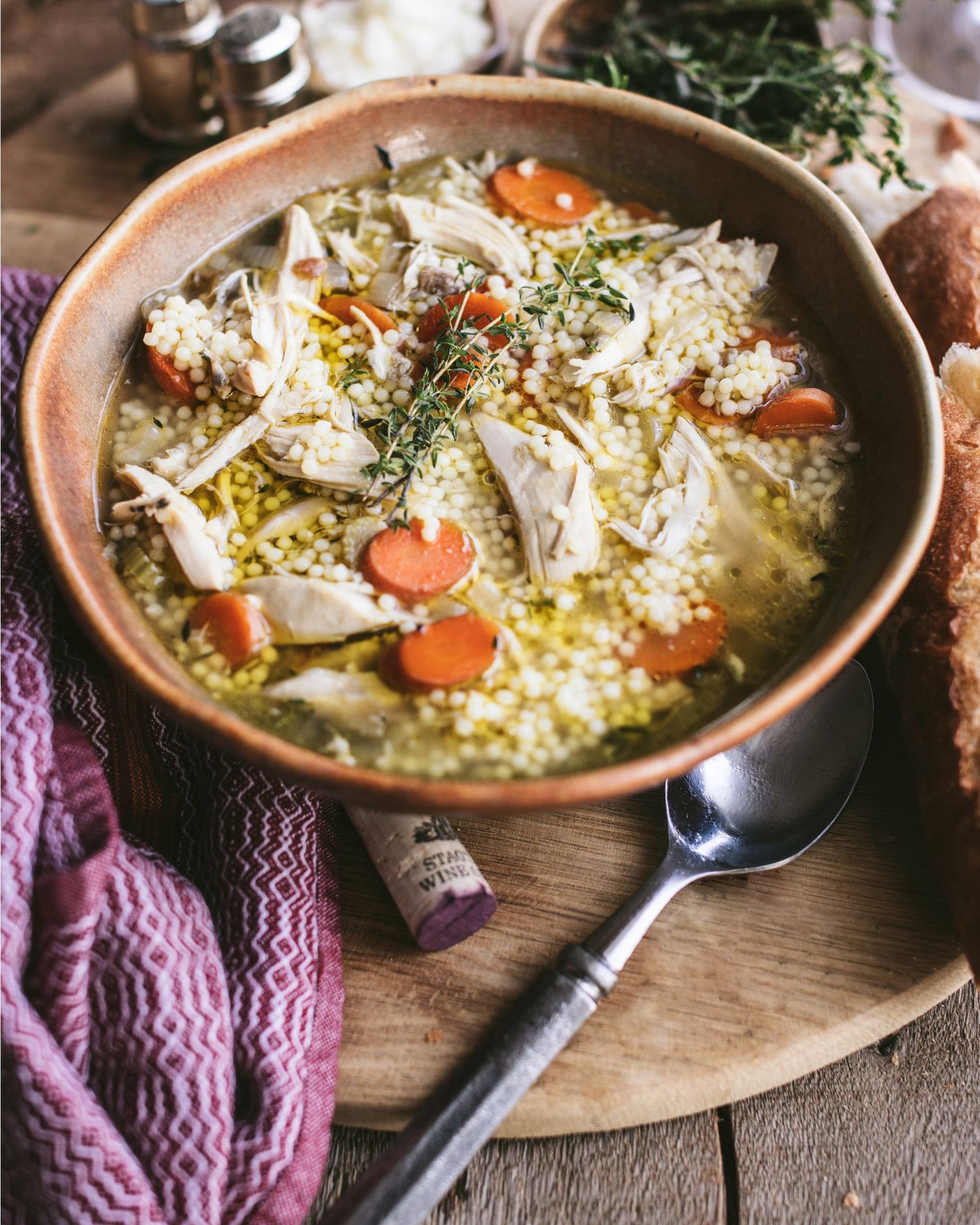 Comforting chicken soup with pearl couscous, sliced carrots, and fresh thyme in a handmade ceramic bowl.
