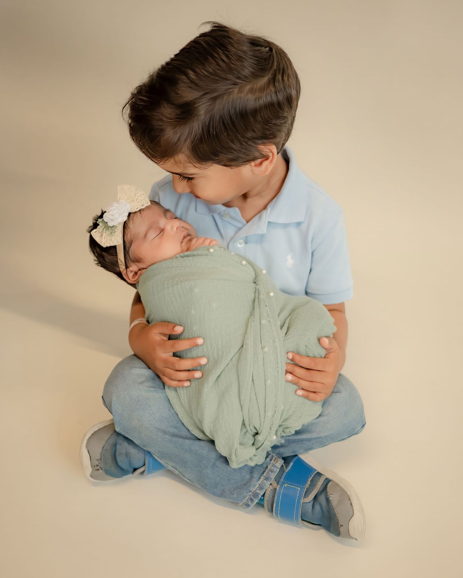 Tender moment between siblings as older brother holds newborn wrapped in mint green.