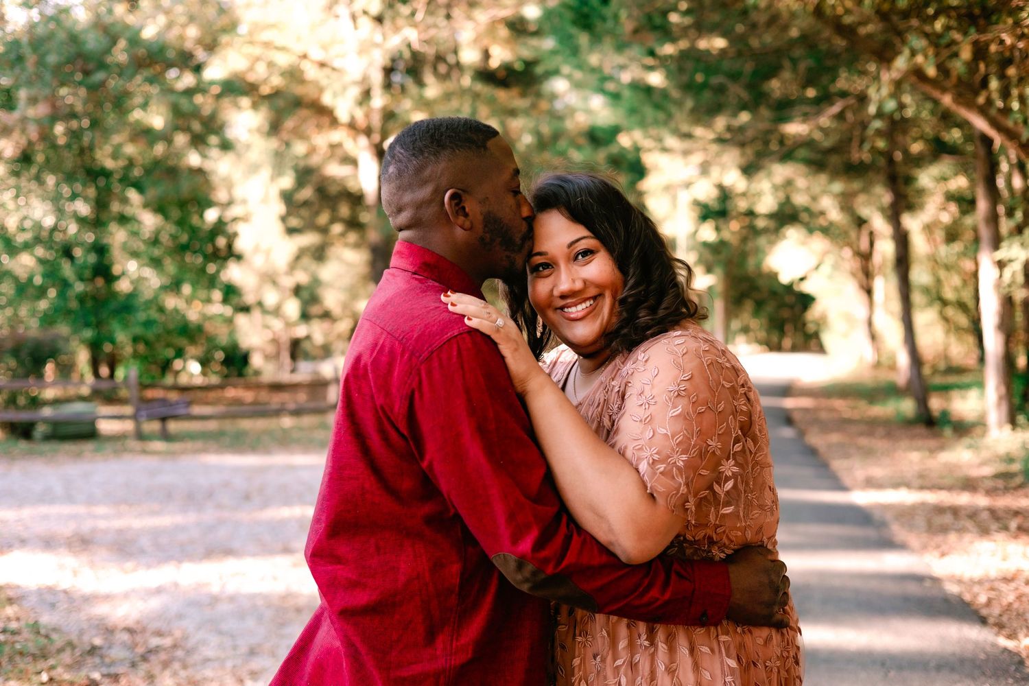 Smiling woman in pink sequin dress embracing man in red shirt on a sunny park path.