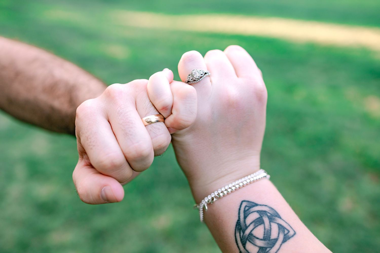 Close-up of couple linking pinky fingers showing engagement rings and a Celtic tattoo.