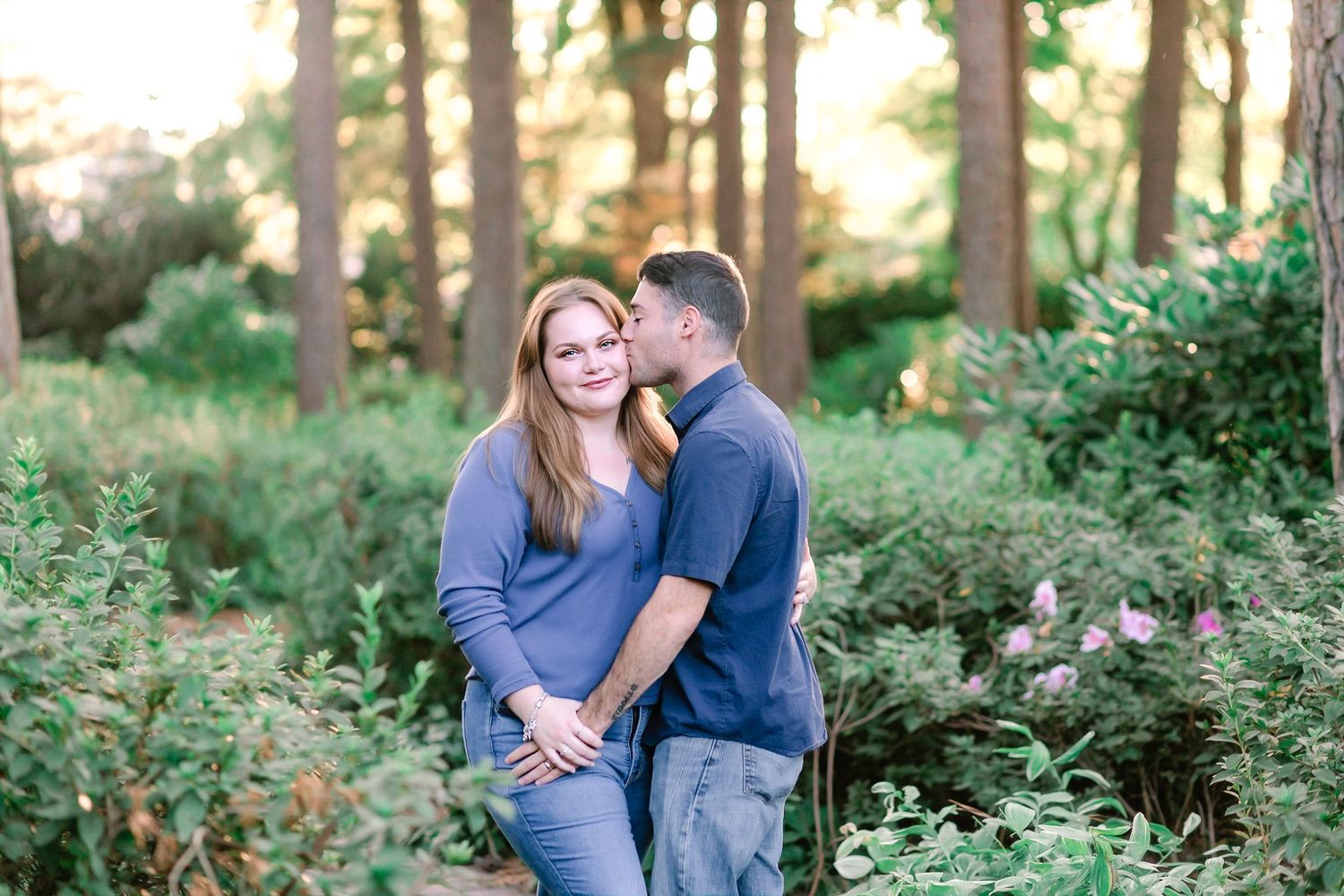 Couple embracing in a lush garden forest setting during golden hour light.