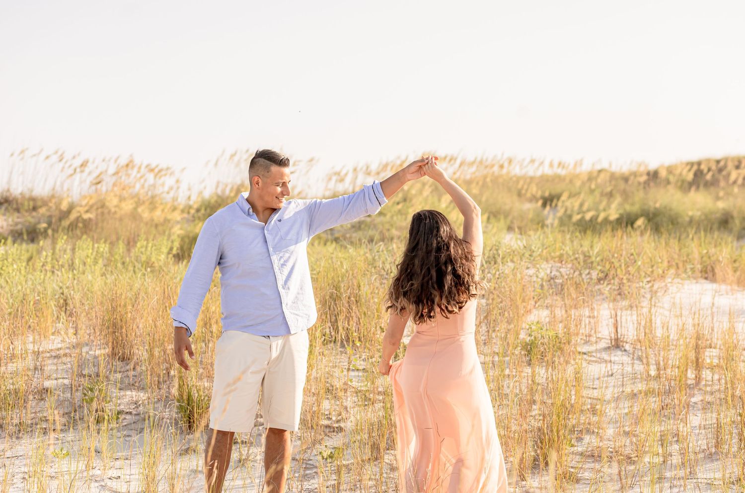 Couple dancing together among golden sea oats on sandy beach dunes at sunset.