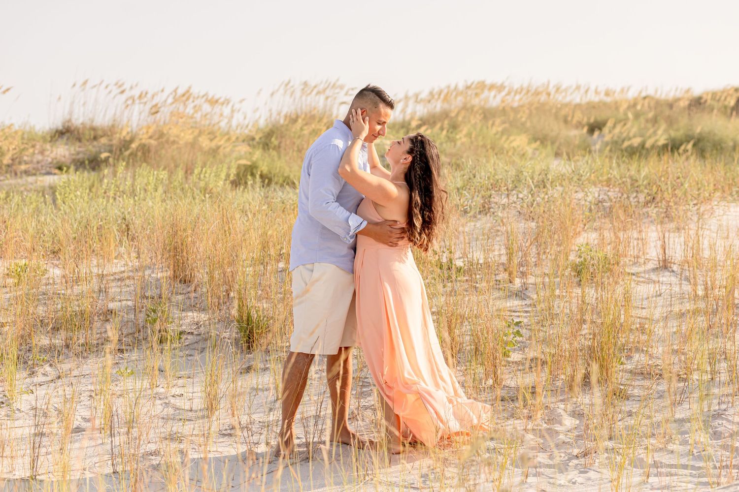 Couple sharing romantic embrace among golden sea oats on white sandy beach dunes.