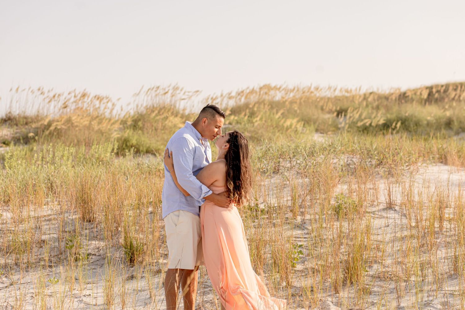 Couple sharing a romantic moment among golden sand dunes and sea grass at sunset beach.