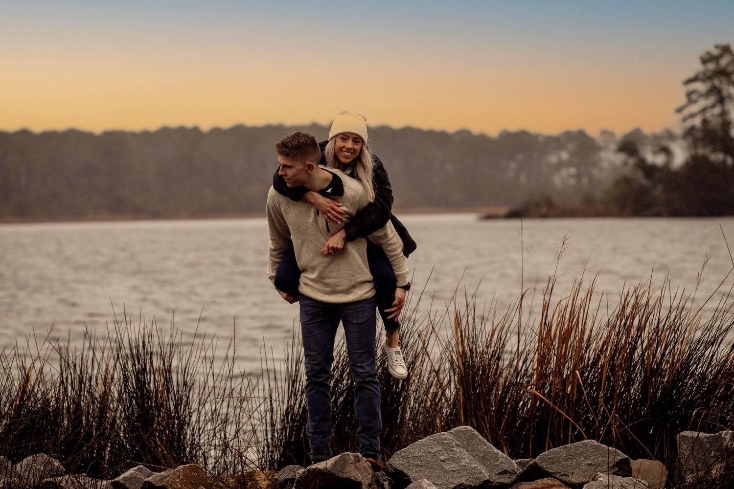 Couple embracing on rocks by lake during golden hour sunset.