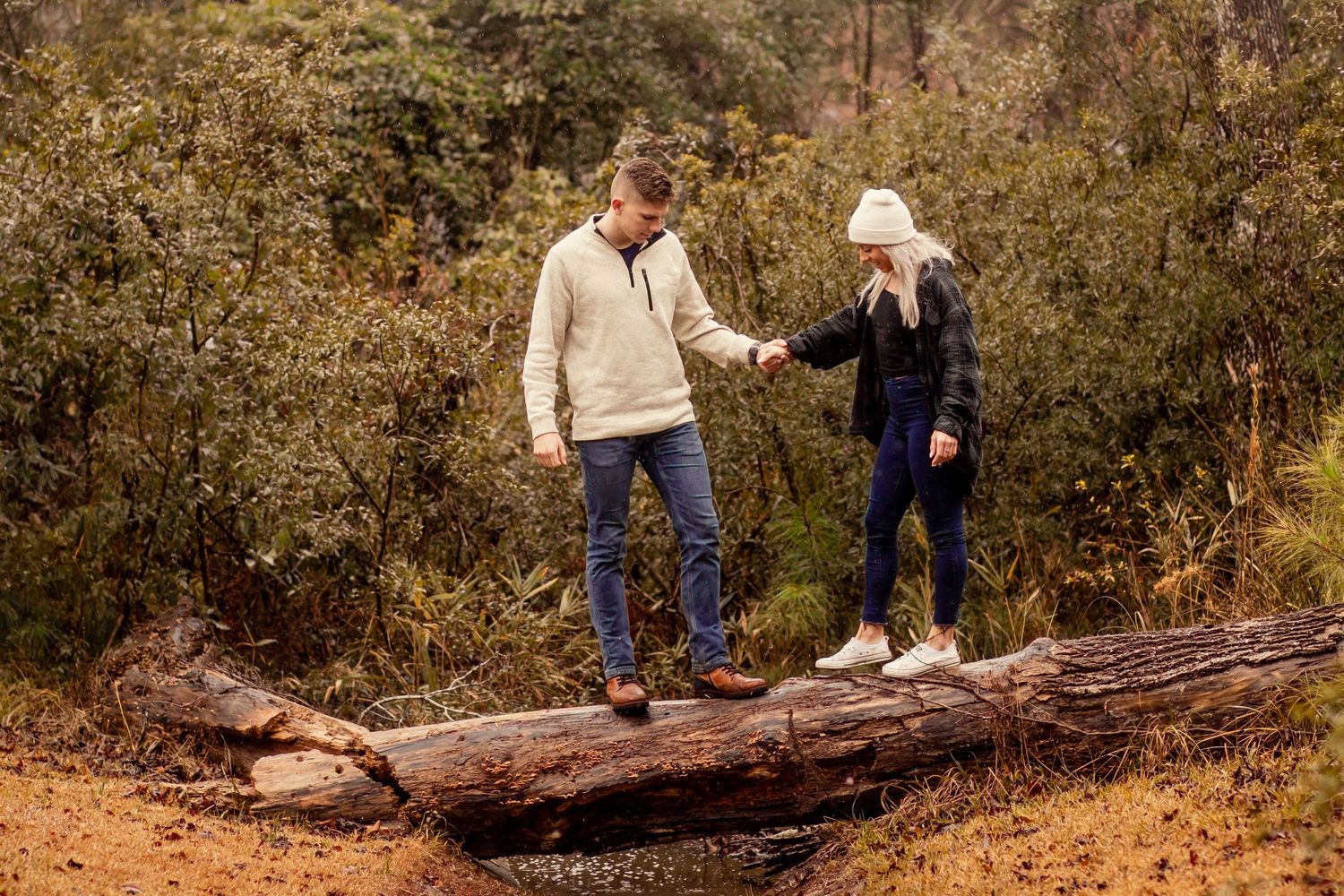 Man helping woman balance while walking across a fallen log in the forest.