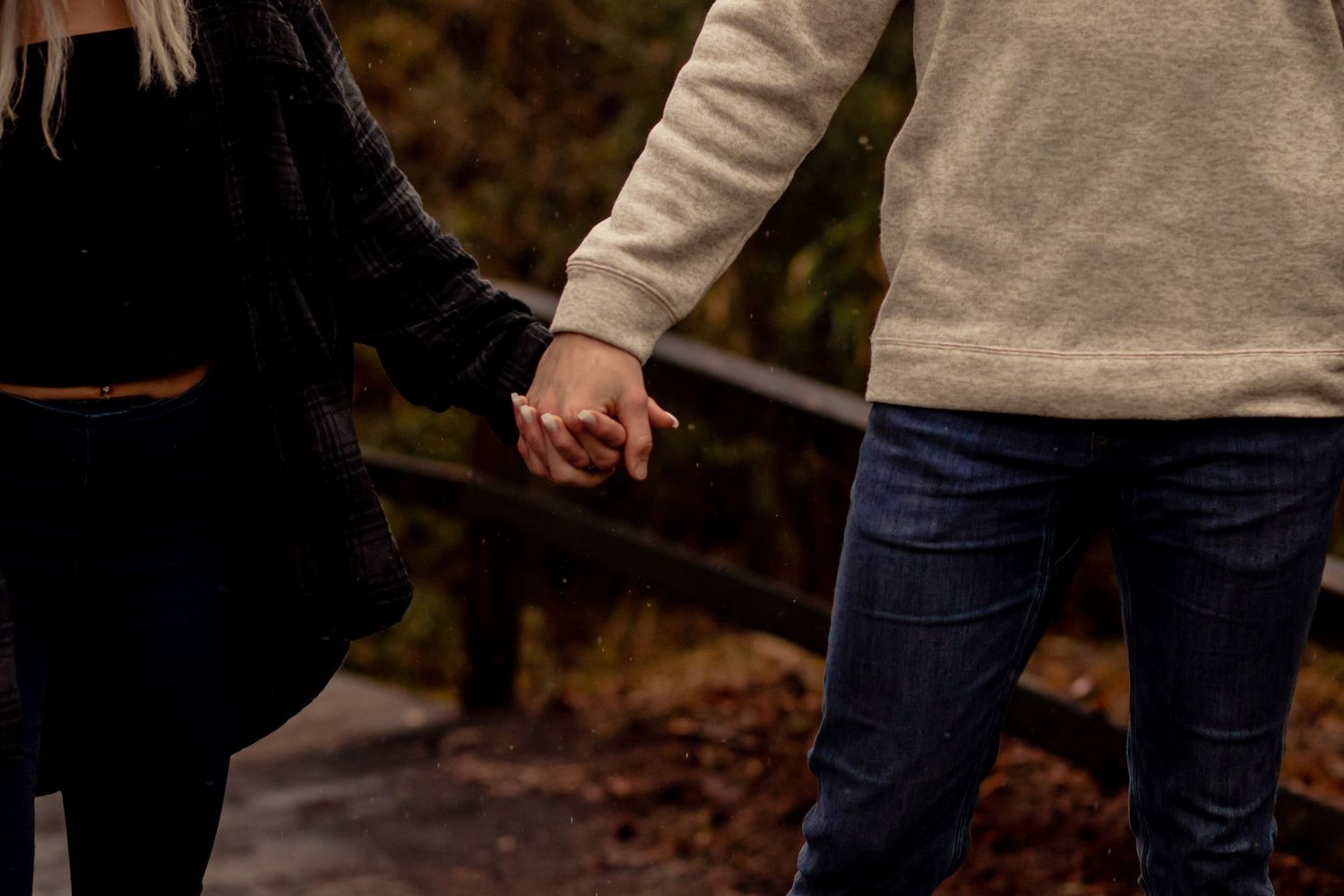 Close-up of a couple holding hands while walking on a rainy path.