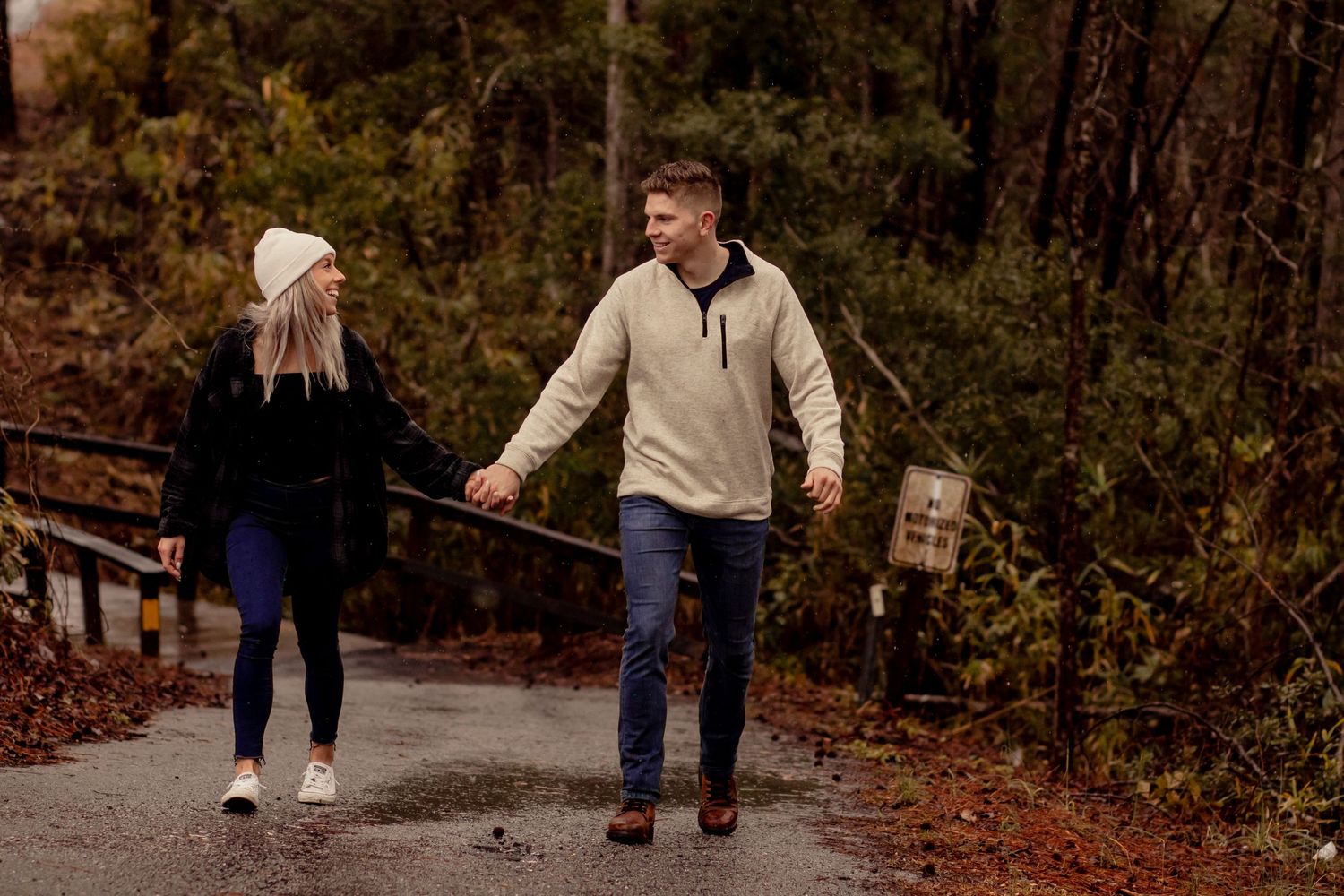 Couple laughing and holding hands while walking on a rainy forest road.