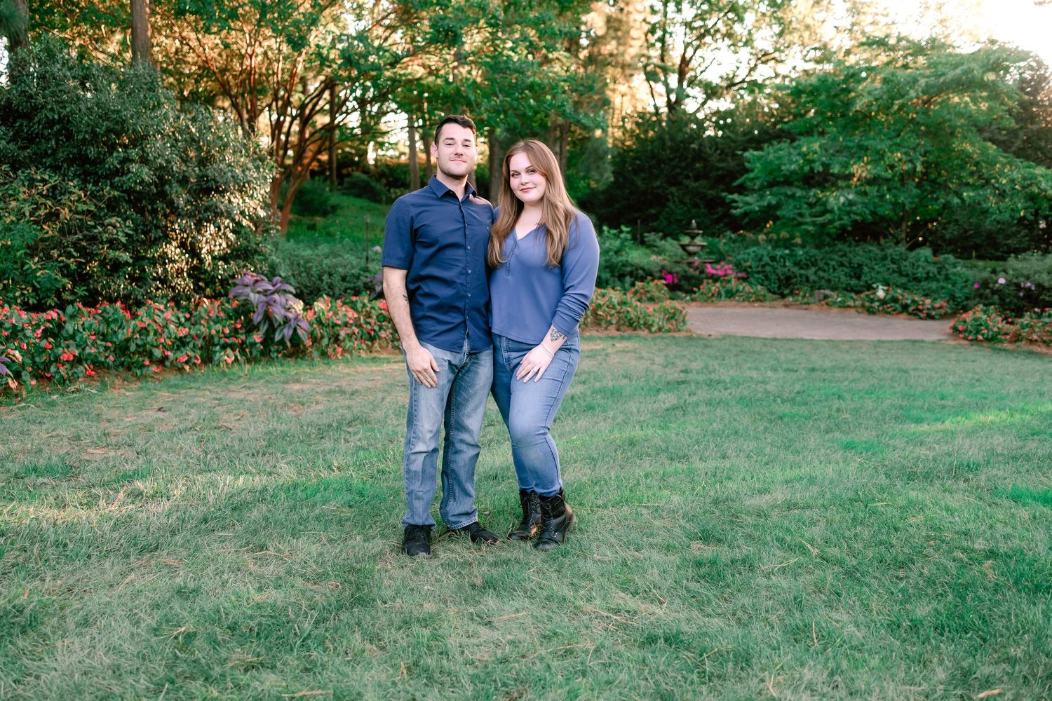 Couple posing together on a green lawn surrounded by colorful garden flowers.