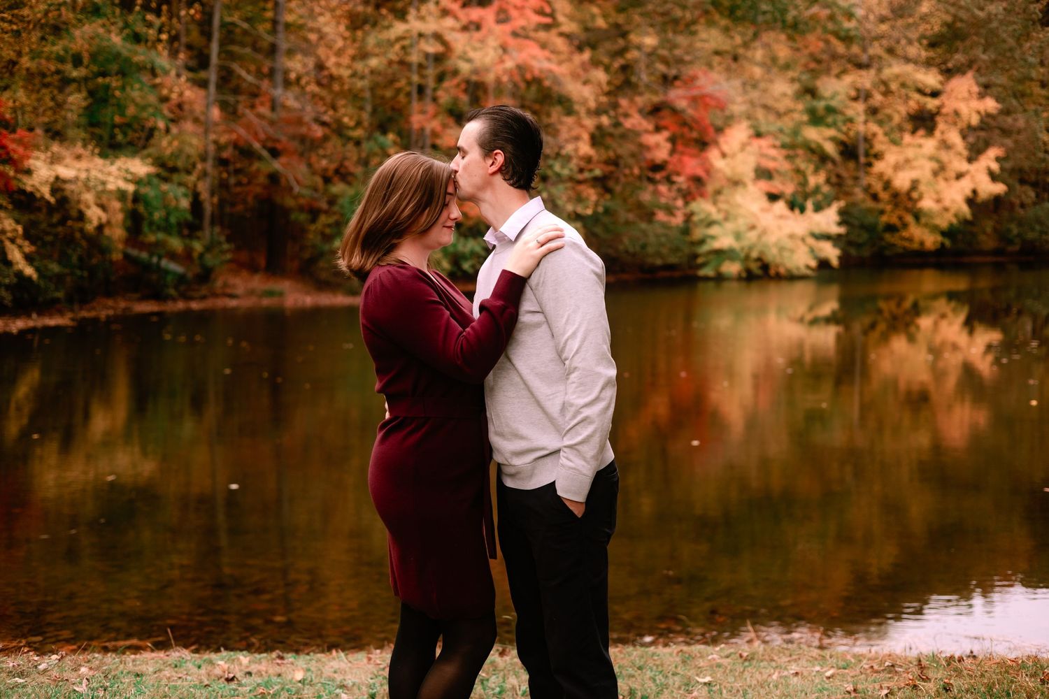 Couple sharing a romantic moment by a pond with colorful fall foliage backdrop.
