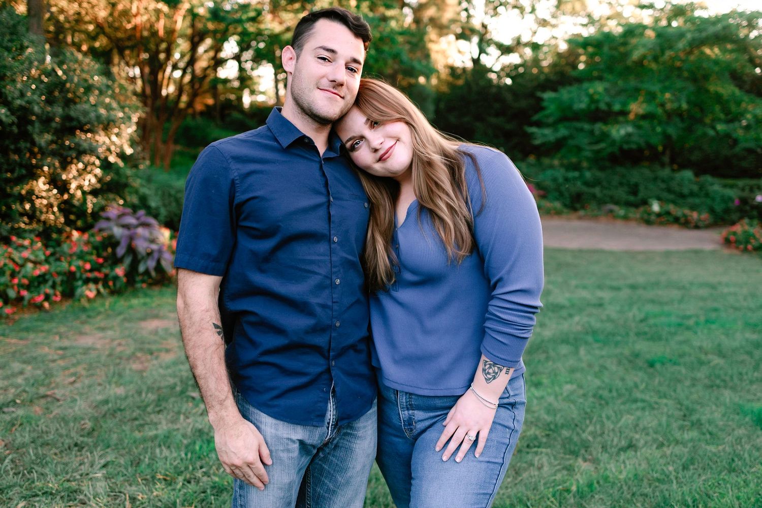 Couple smiling and embracing outdoors in a garden setting during warm evening light.