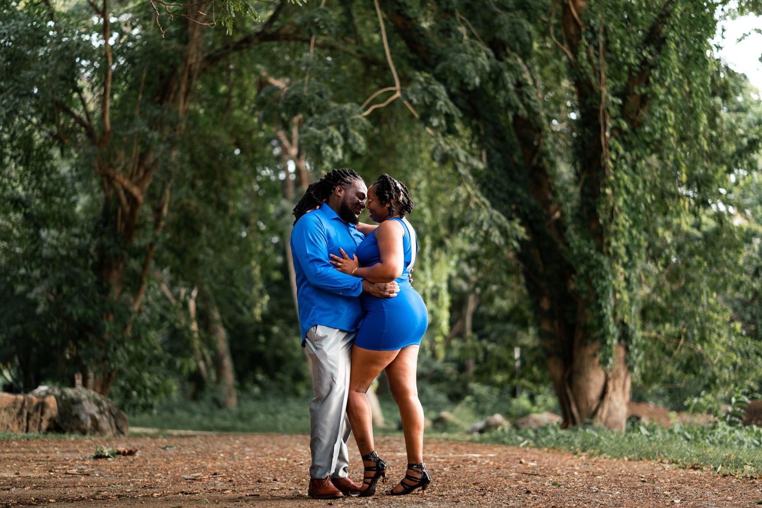 A couple in matching blue outfits embraces on a forest path.