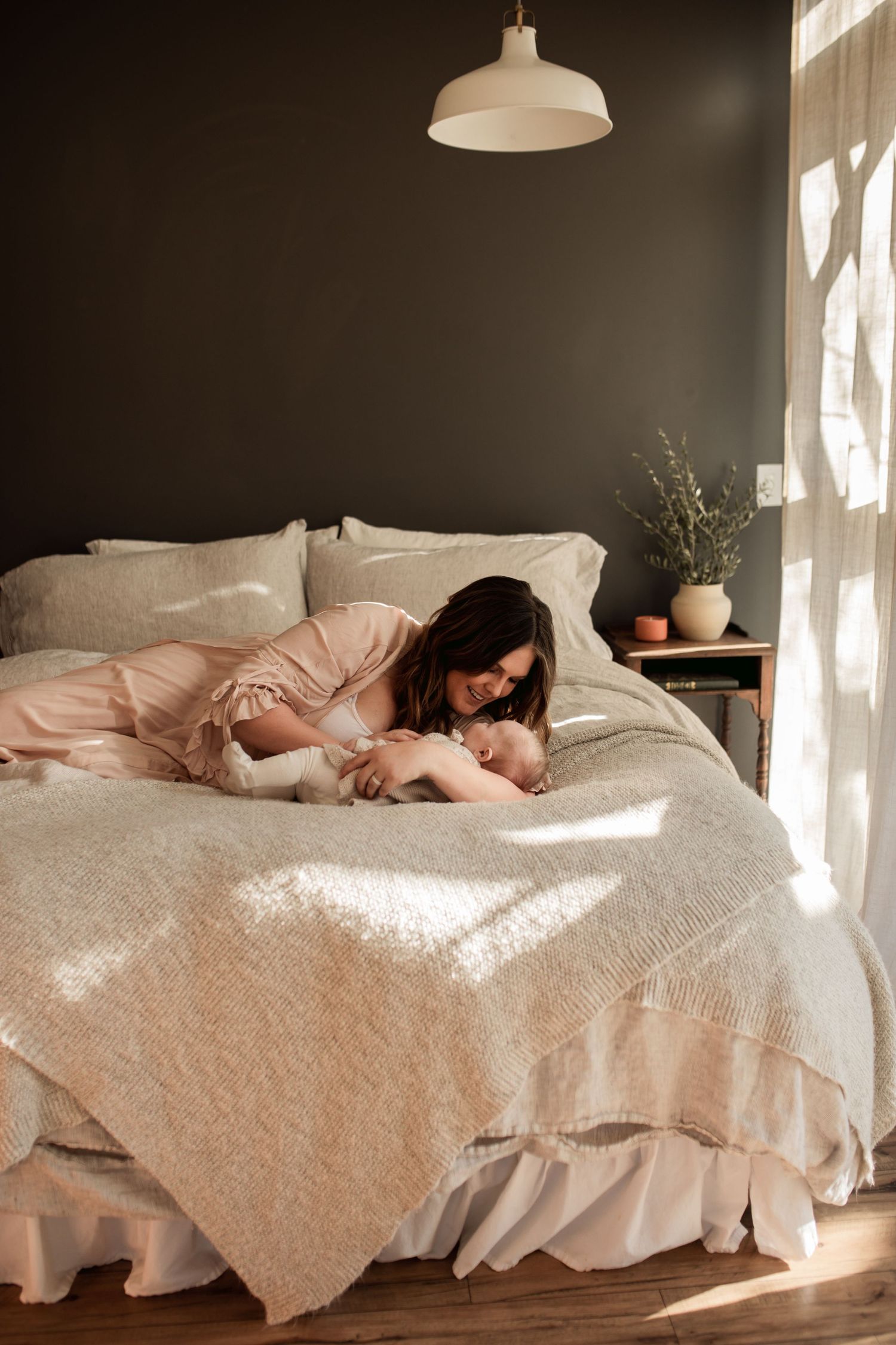 Tender moment between parent and baby on white bed with sunlight streaming through window.