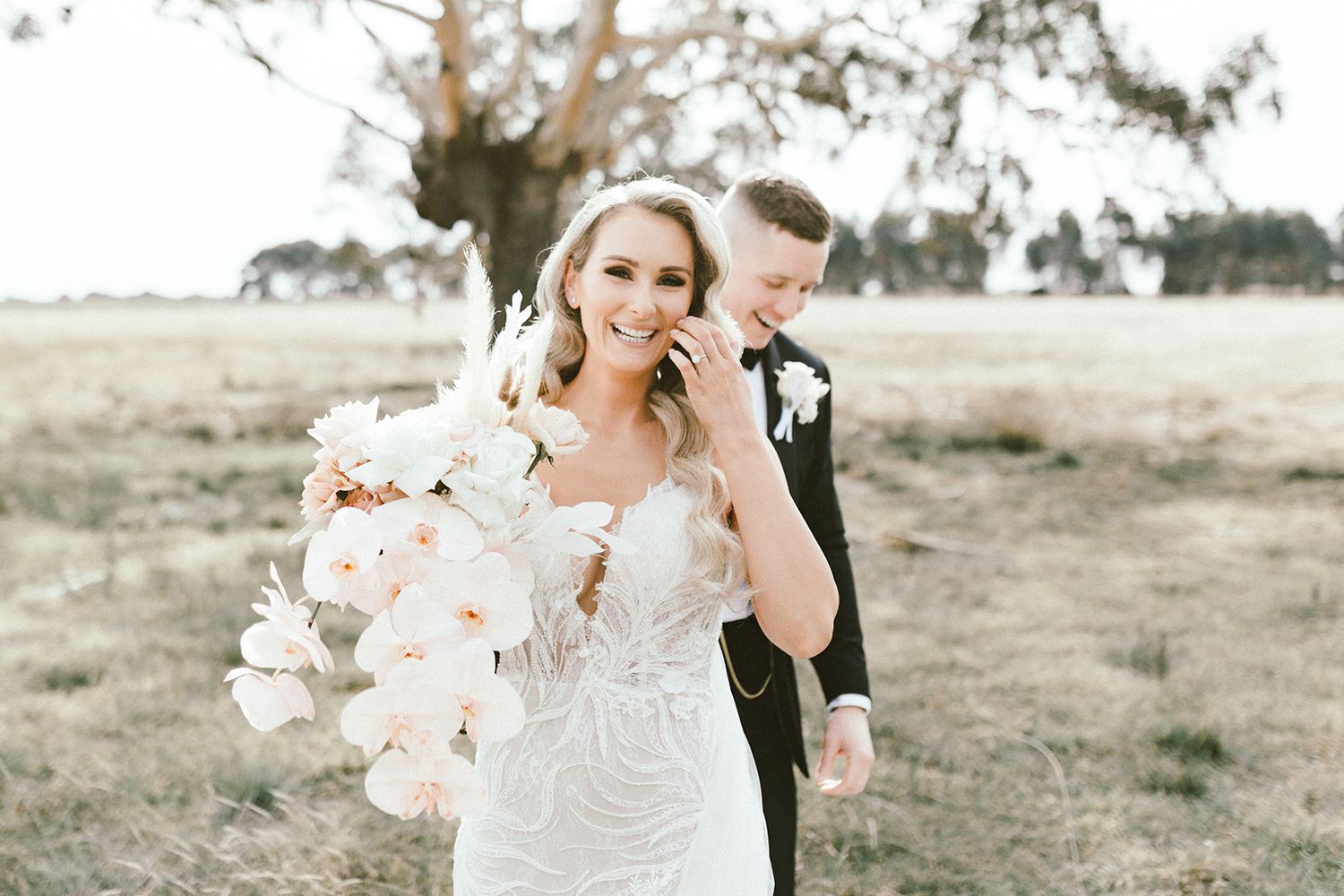 Elegant bride holds peach bouquet in outdoor setting with soft lighting.