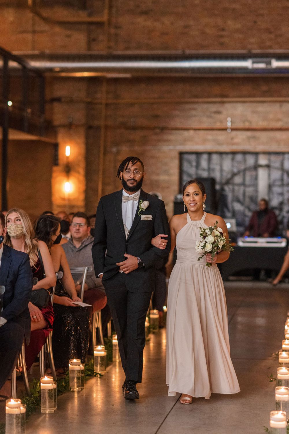 Wedding party members proceeding down an aisle lined with glowing candles.