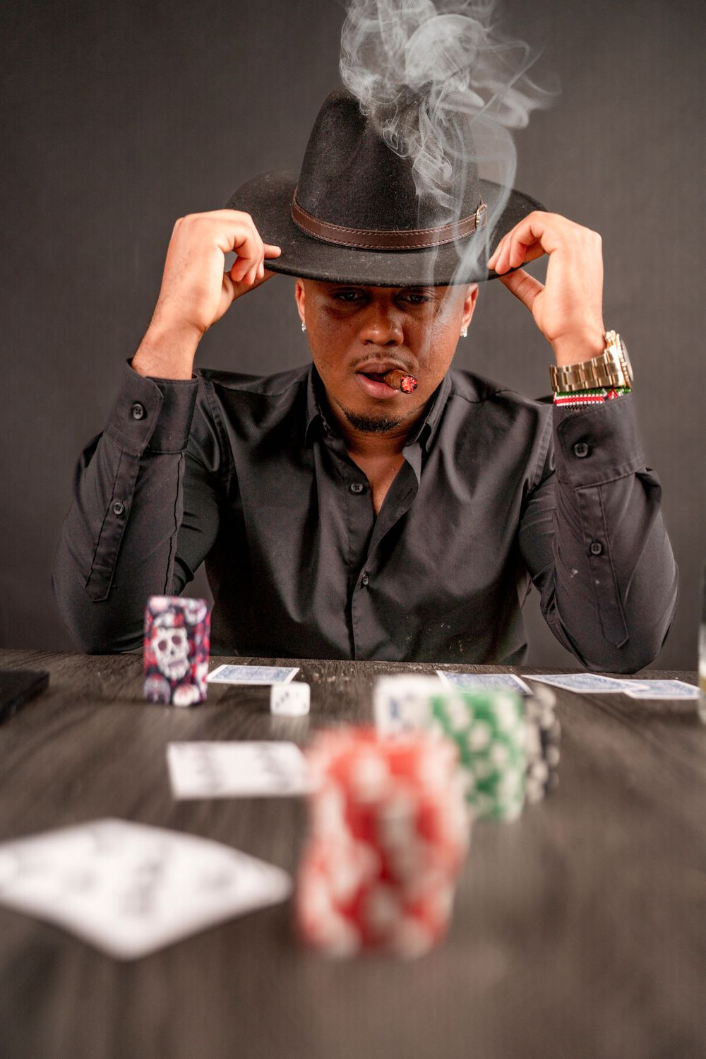 Moody poker game setup with fedora hat, smoke and casino chips on dark table.
