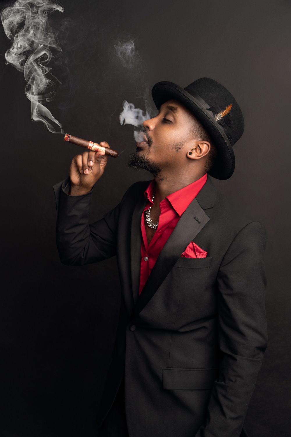 Stylish side profile with fedora hat and cigar smoke in formal attire against black background.