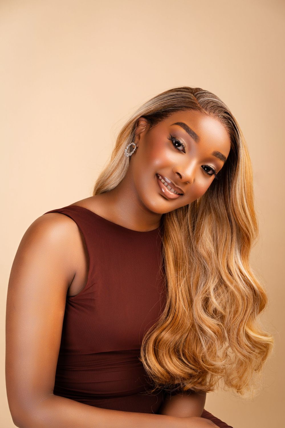 Beauty portrait featuring long blonde wavy hair and brown sleeveless top against neutral background.