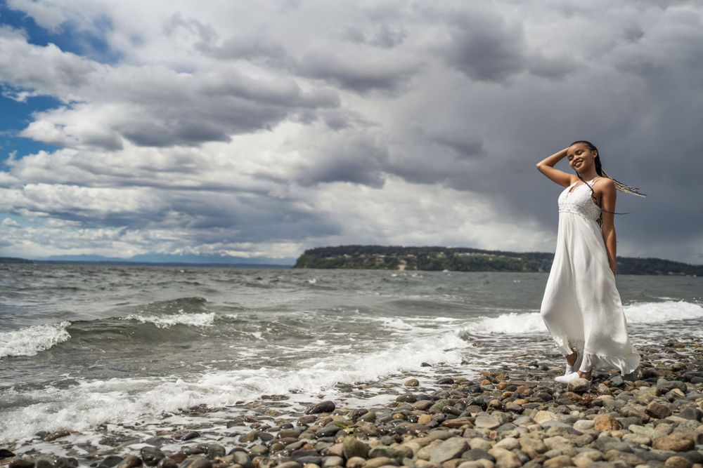 Ethereal beach photograph with flowing white dress against dramatic cloudy seascape.
