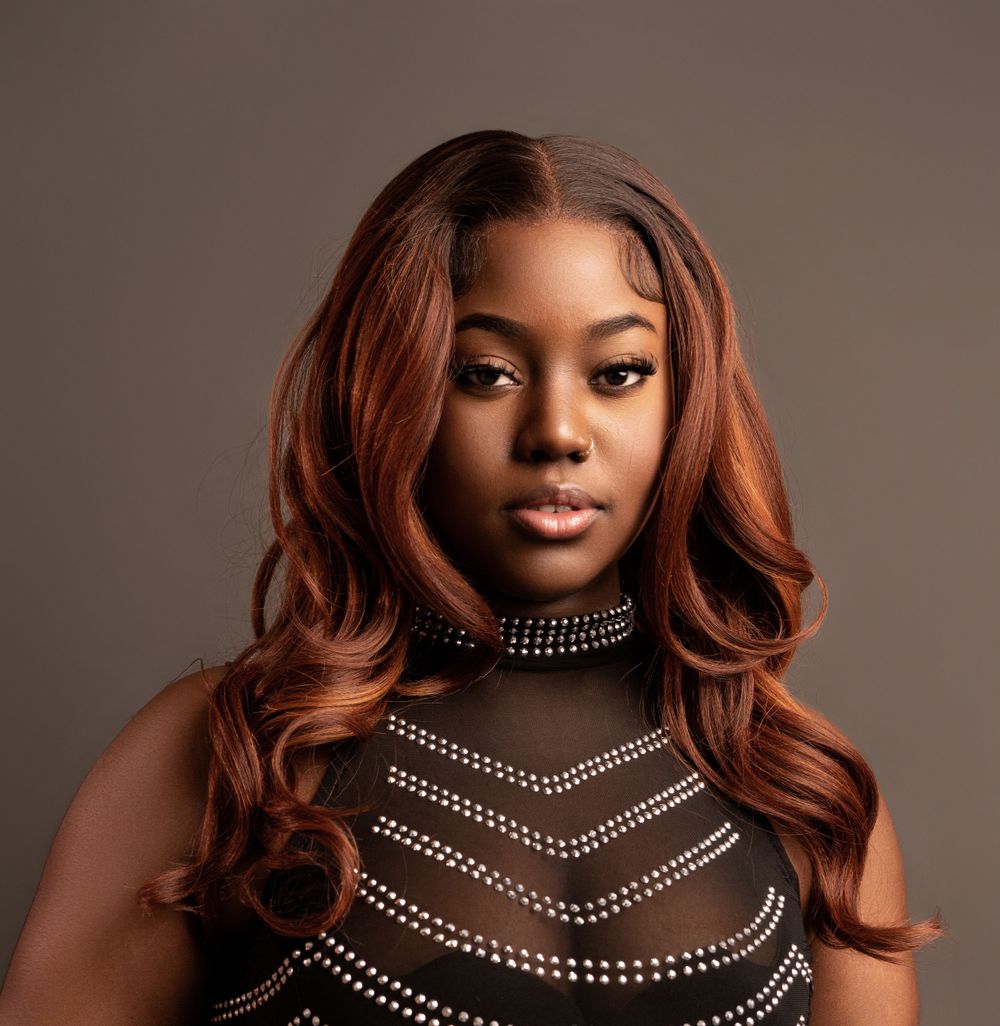 Glamour portrait featuring auburn waves and a rhinestone-decorated black high neck top against brown background.