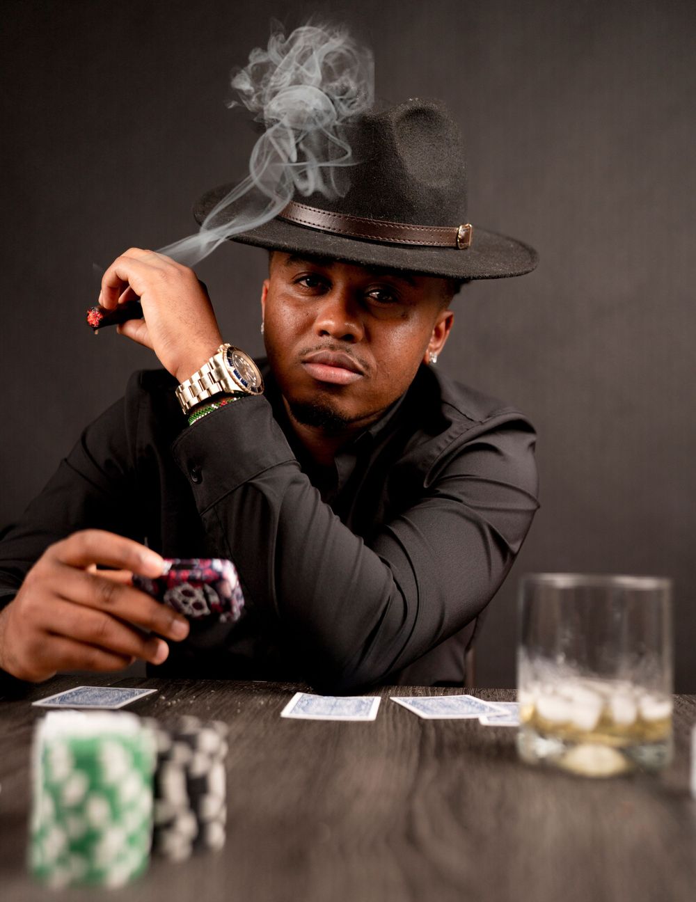 Dramatic poker scene with smoke, hat, cards and chips on wooden table.