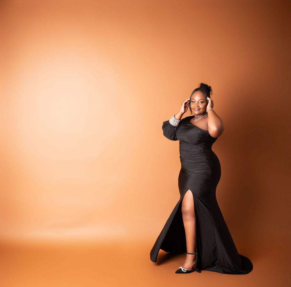 Glamorous portrait in a form-fitting black evening gown against an orange backdrop.