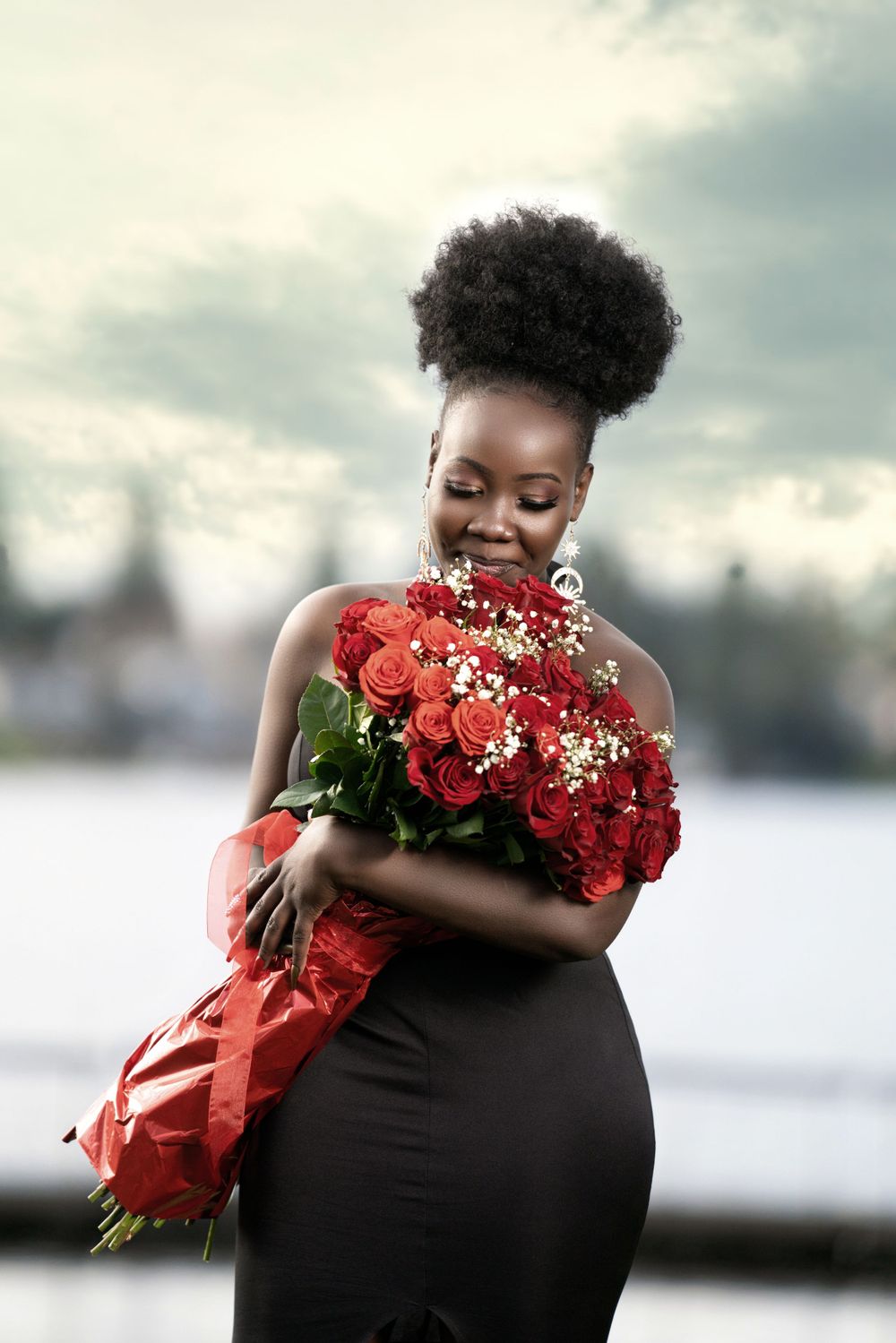 A woman in a black dress holds a stunning bouquet of red roses outdoors.