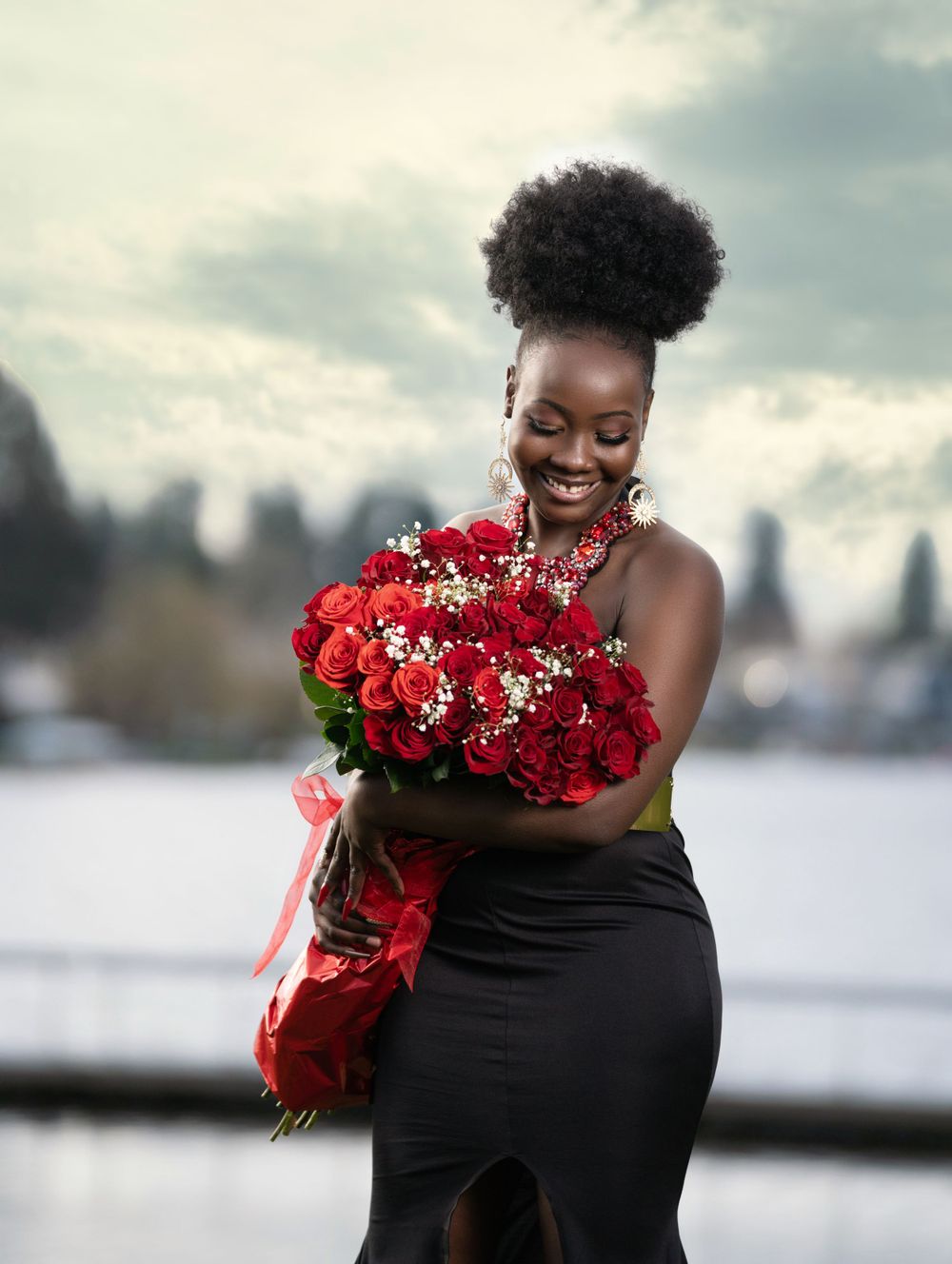 Joyful outdoor portrait with a beautiful bouquet of red roses against a cloudy sky.