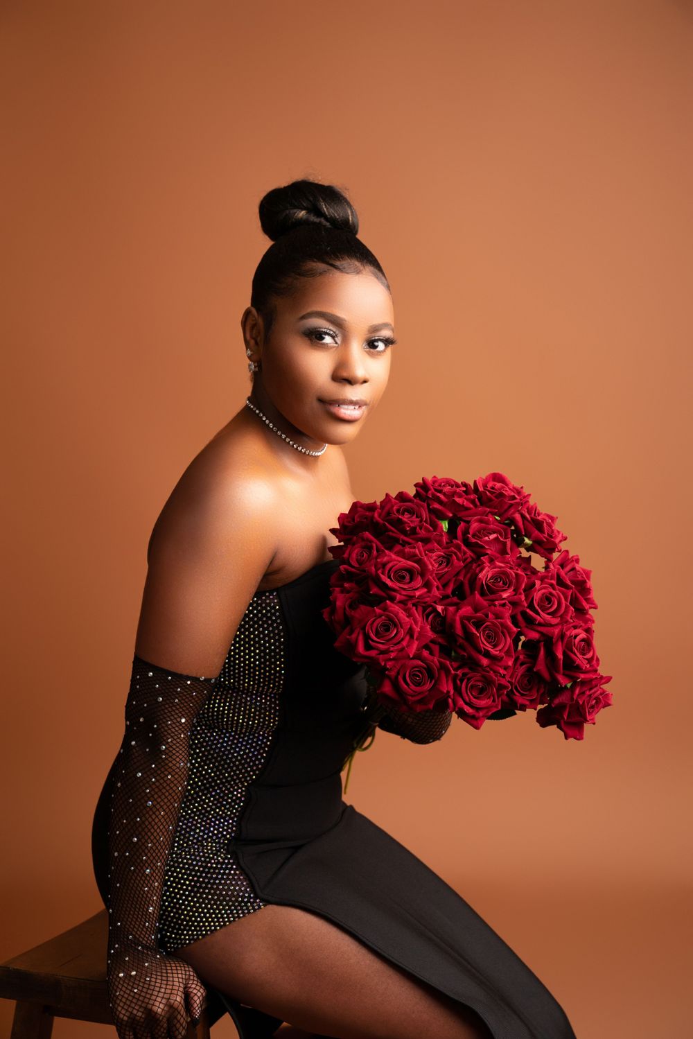 Elegant portrait with burgundy roses and sparkly black dress against warm background.