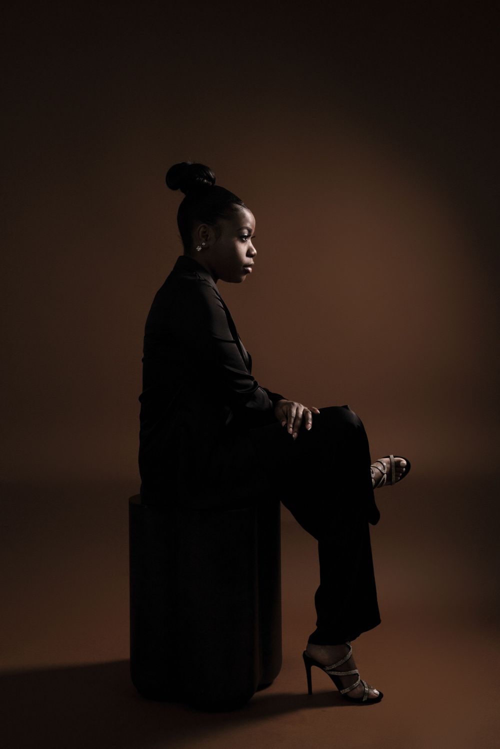 Dramatic side profile portrait in black attire against dark brown background.