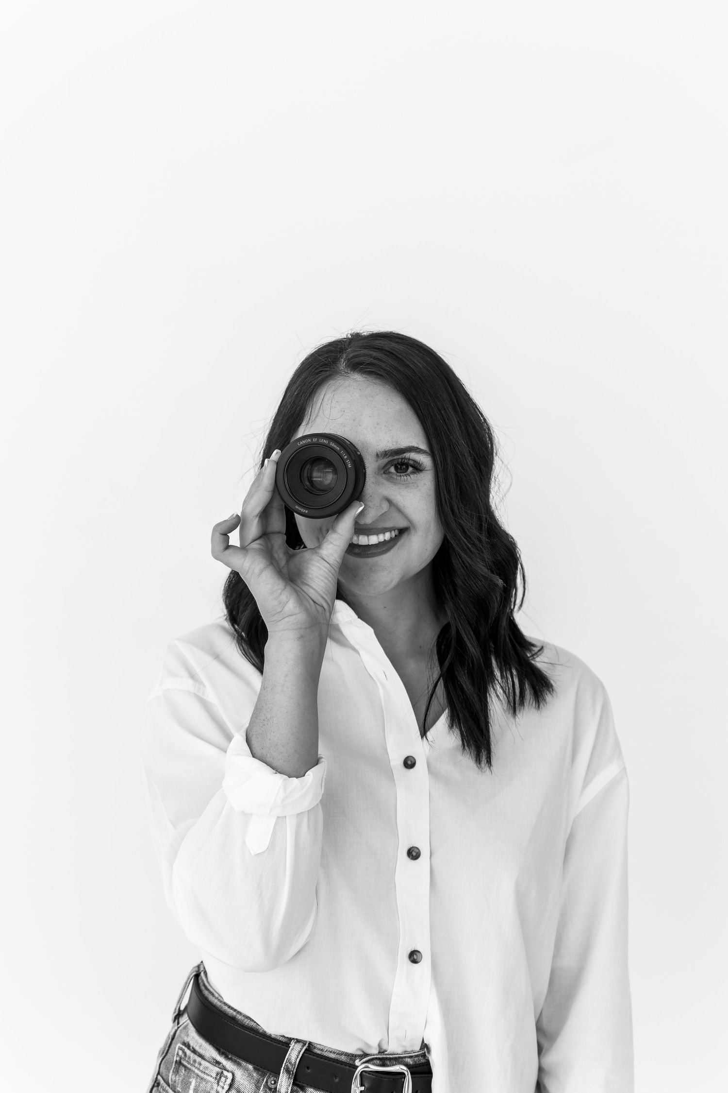 Photographer in white button-down shirt playfully looks through camera lens.