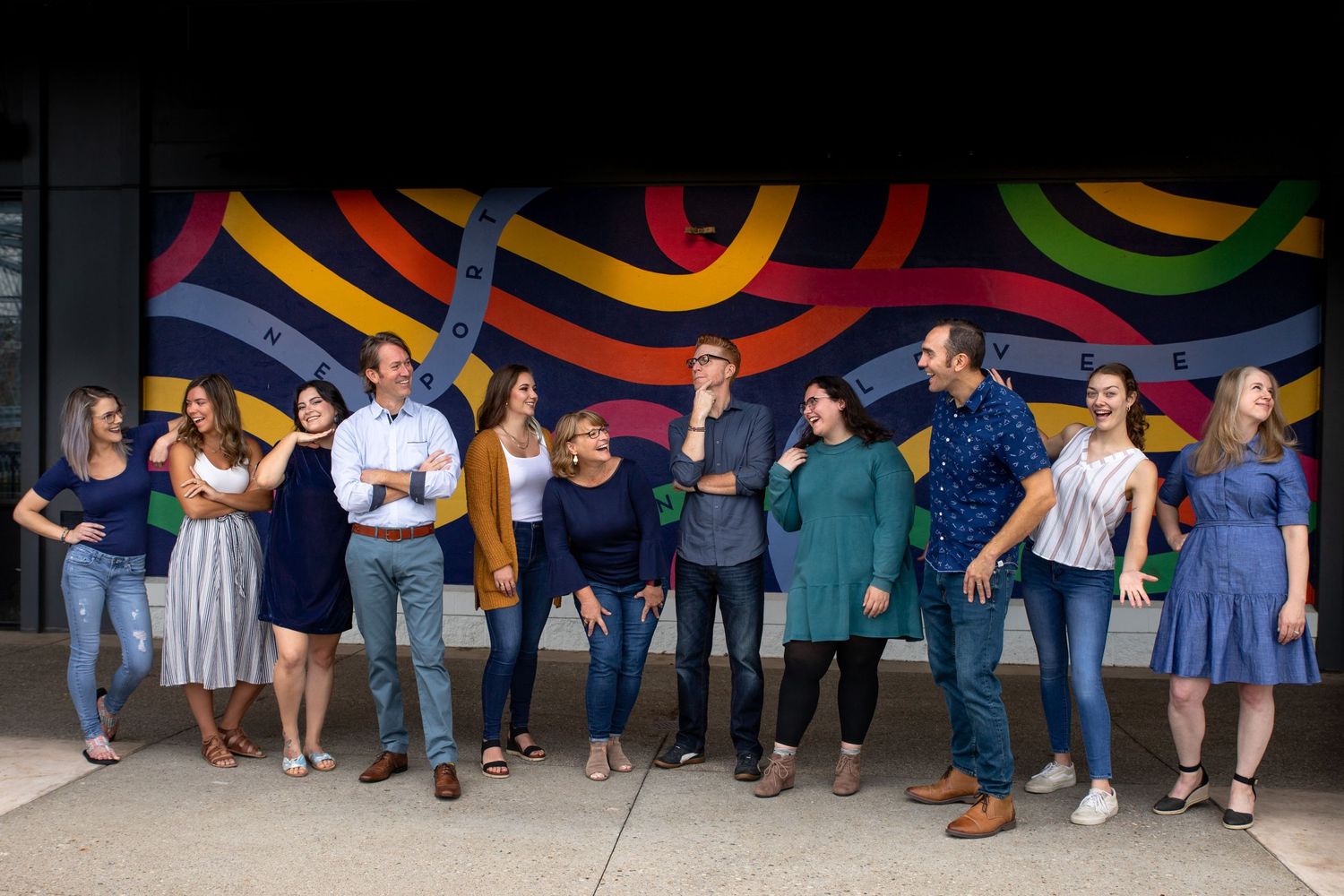 Diverse group poses enthusiastically in front of colorful striped wall mural.