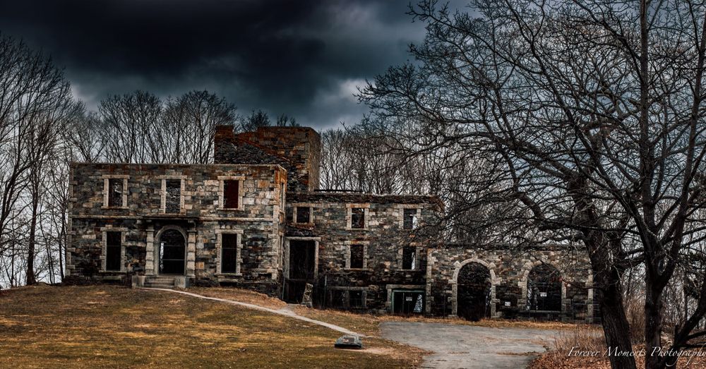 Abandoned stone mansion with dark stormy sky and bare trees in winter.
