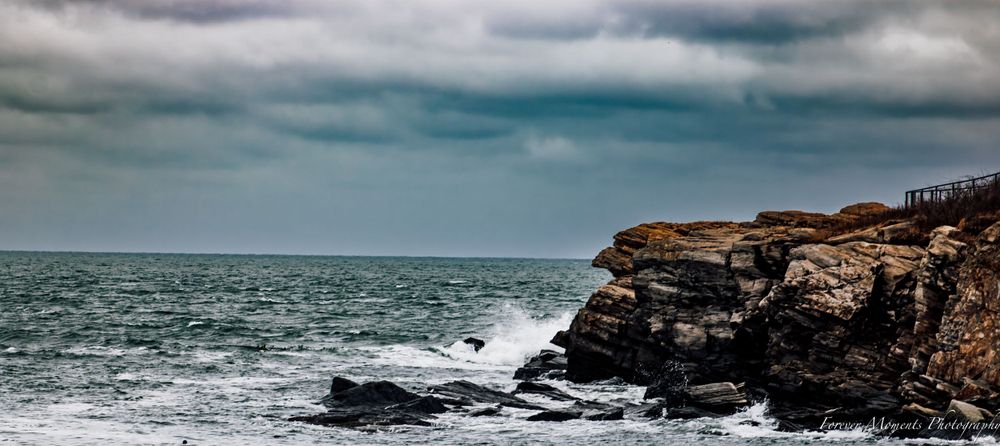 Dramatic seascape with waves crashing against rocky cliffs under stormy skies.