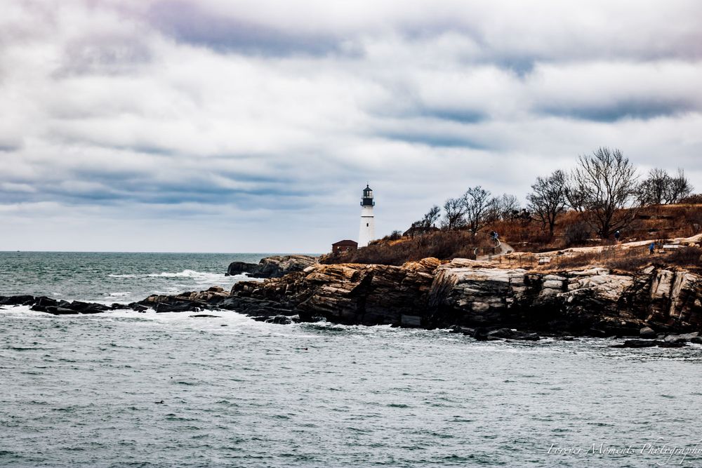 Dramatic coastal lighthouse scene with crashing waves against rocky cliffs under cloudy skies.
