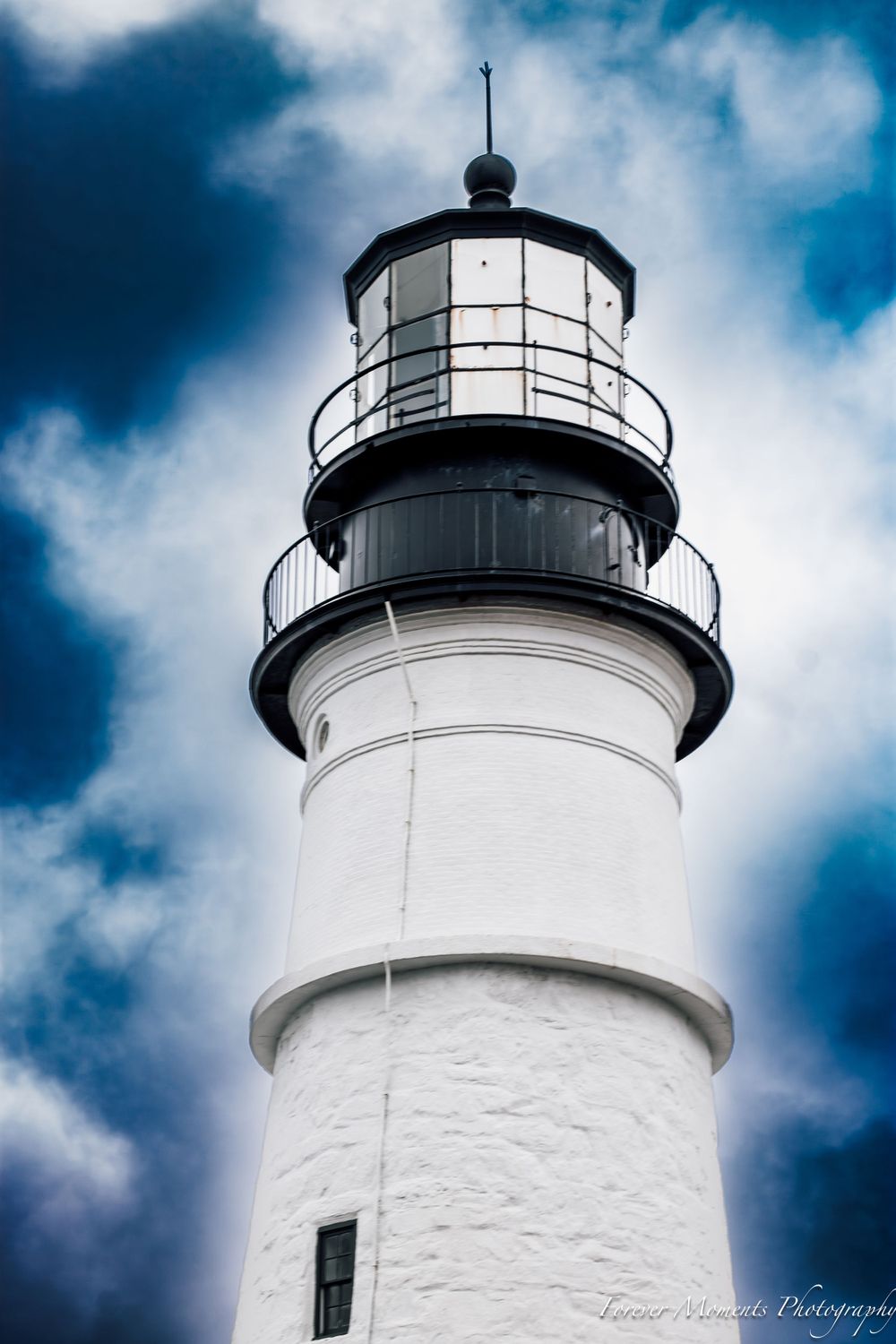 Classic white lighthouse tower against dramatic blue cloudy sky.