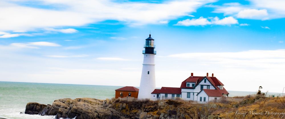 Panoramic view of Portland Head Light station with white lighthouse tower and red-roofed buildings.