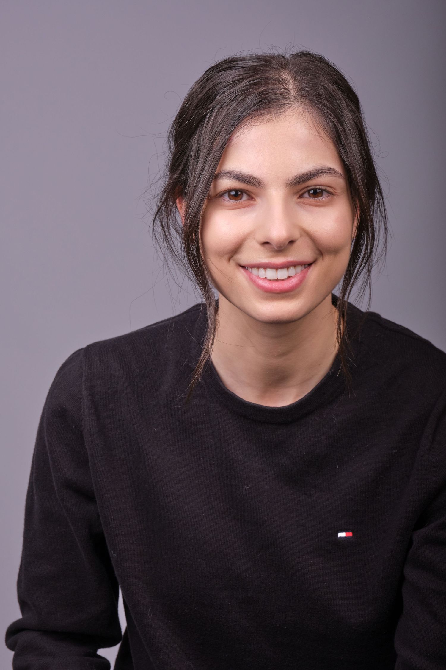 Portrait of person in black Tommy Hilfiger sweater with natural makeup and pulled back hair.