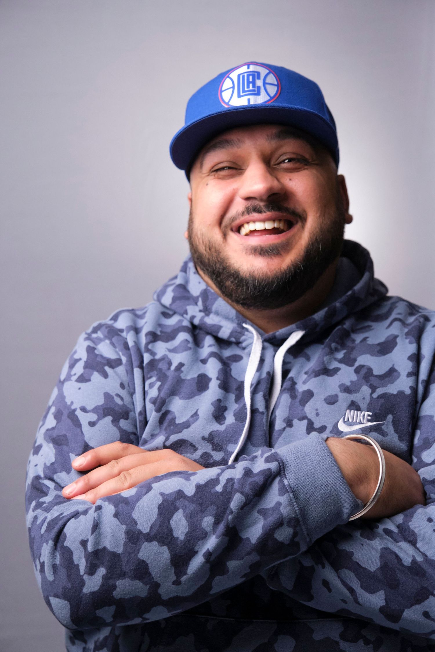 Person wearing blue baseball cap and camouflage Nike hoodie smiles at camera.