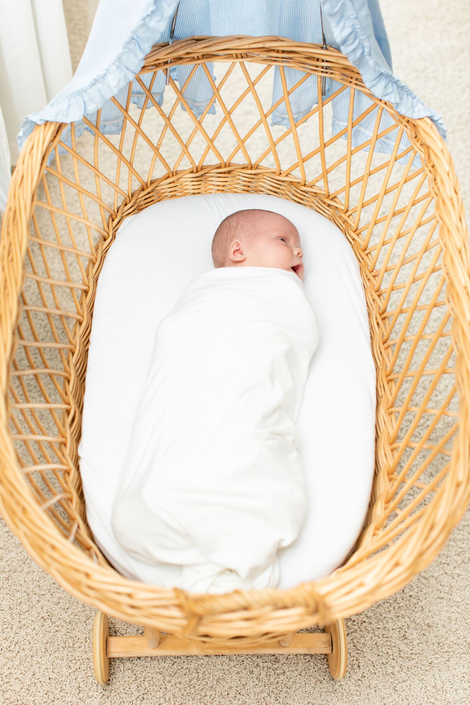 Sleeping newborn swaddled in white blanket inside vintage wicker bassinet.