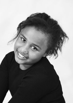 Black and white portrait of a smiling young girl with curly hair wearing a dark top.