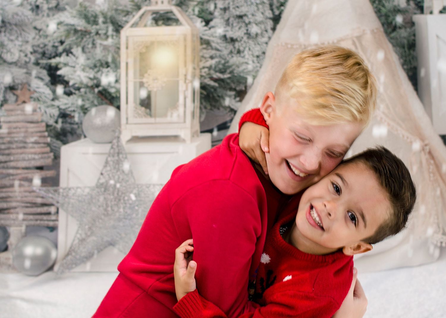 Two young boys in matching red outfits share a joyful hug during a Christmas photo session.
