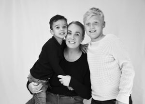 Black and white portrait of a smiling mother with her two young sons in a studio setting.