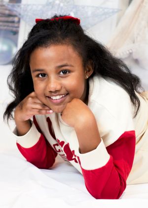 Happy young girl with long dark hair and red bow smiling while lying down in festive holiday setting.
