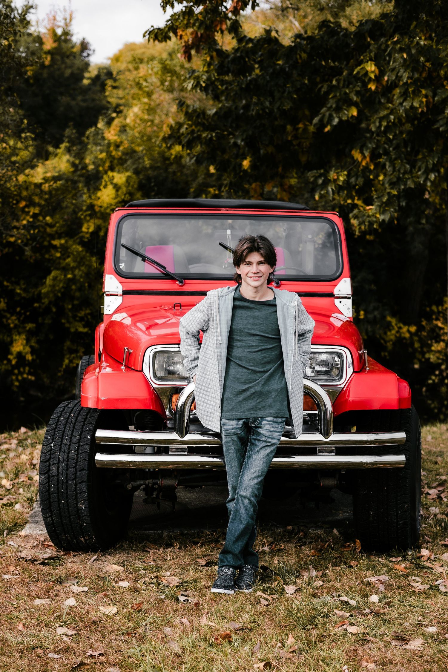 Person leaning against bright red vintage Jeep outdoors in fall setting.