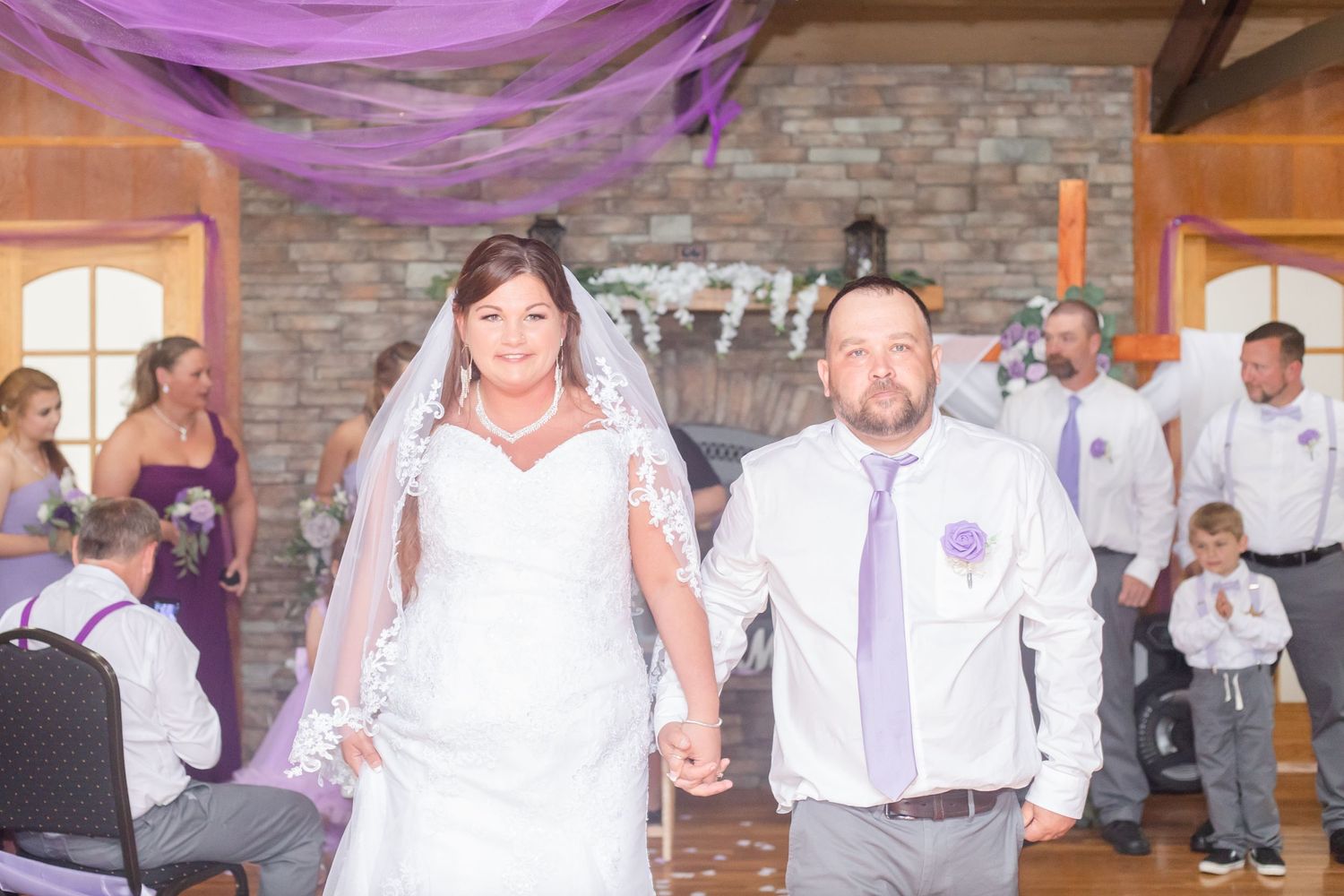 Wedding reception venue decorated with purple lighting and stone wall backdrop.